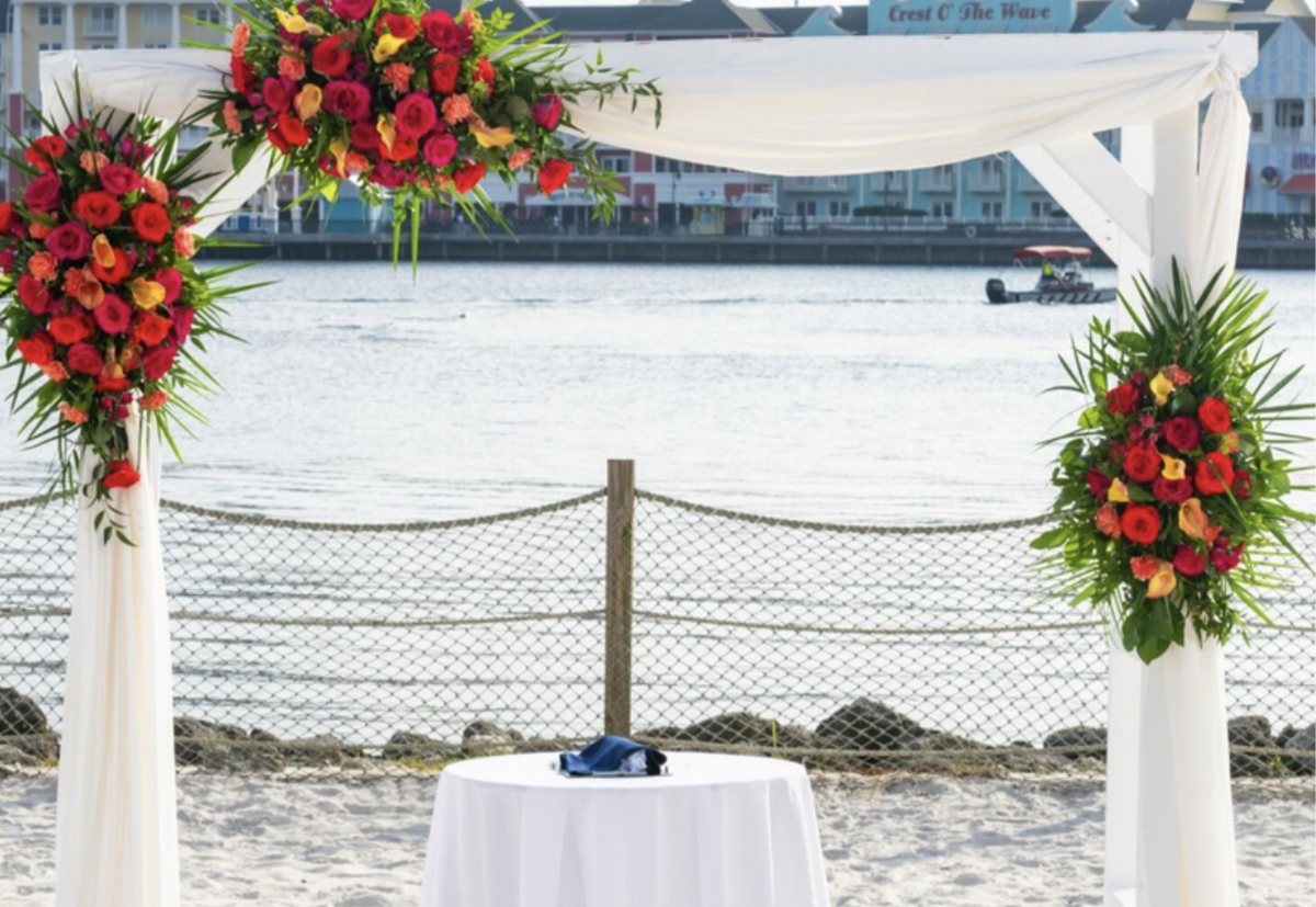 White draped chuppah with red floral sprays on a beach