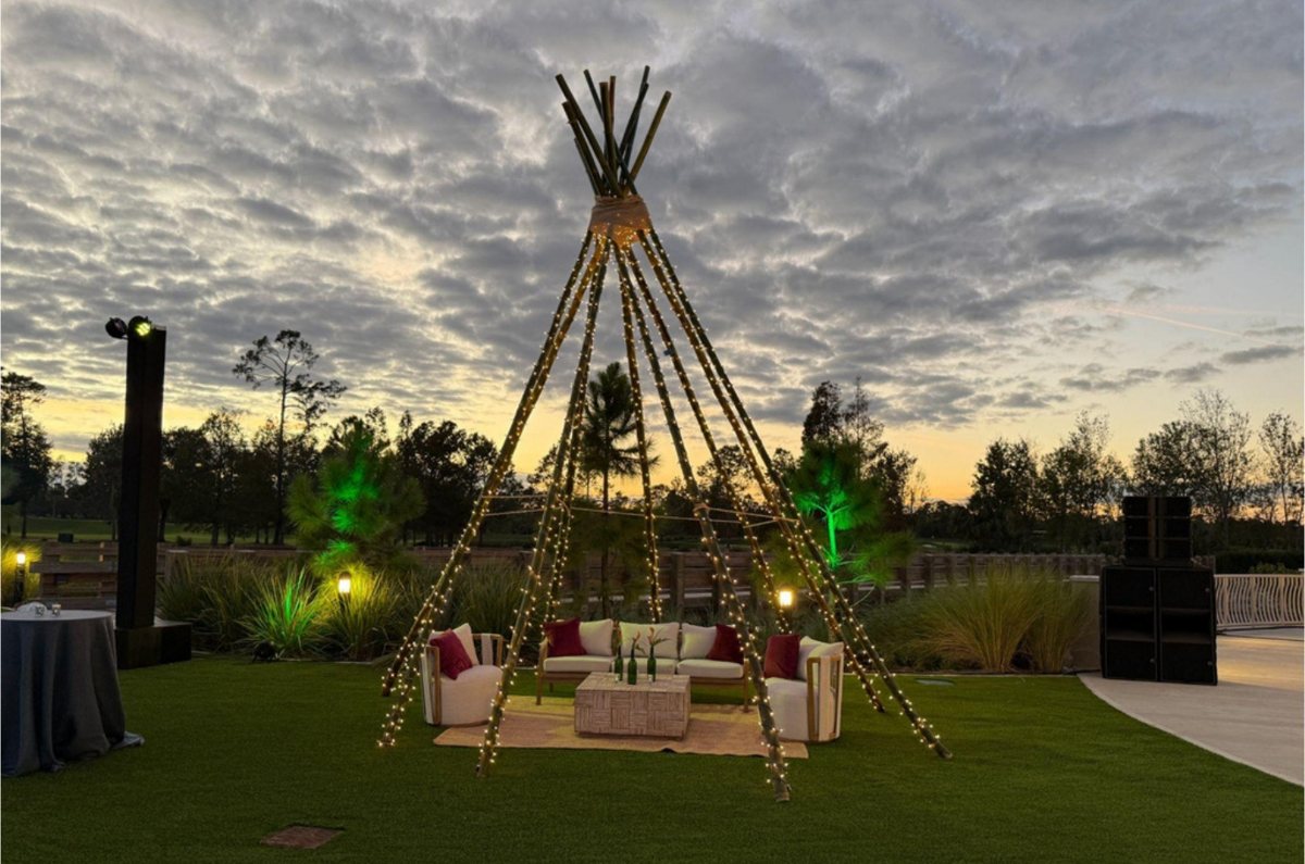 Lighted teepee framed structure on a lawn at dusk